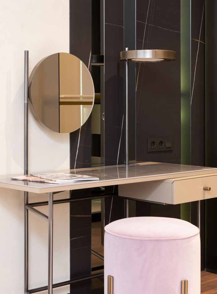 Offerings Soft padded stool near trendy vanity table with rounded mirror and stylish lamp