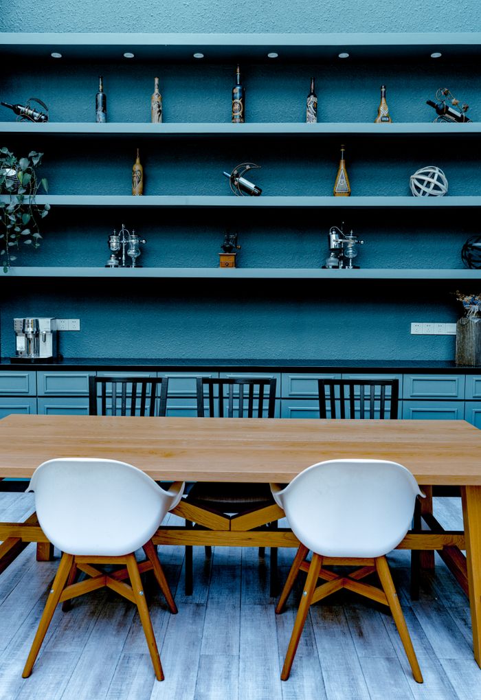 Interior of modern kitchen with wooden table and chairs against blue abinets with shelves